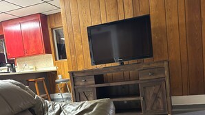 Ein Wohnzimmer mit einer Ledersofa, Holzpaneelen, einem Flachbildfernseher und einer Küche mit roten Schränken.