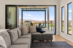 A modern living room with a large gray sectional sofa, a black patterned rug, and a view of a pool and mountains. - Lagoon Landing: Private Pool + Beach/Lagoon Front (St. George)