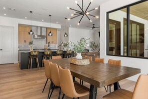 A modern kitchen with wooden cabinets, a central island, pendant lighting, and a dining area with a wooden table and chairs. - Lagoon Landing: Private Pool + Beach/Lagoon Front (St. George)