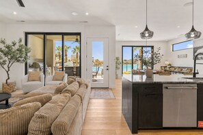 A modern kitchen with a central island, a dining area with a view of the pool, and a living room with a large sofa and a plant. - Lagoon Landing: Private Pool + Beach/Lagoon Front (St. George)