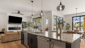 Et moderne køkken med en stor ø, rustfrie stålgadgetter, hængende lamper og et fladskærms-tv.