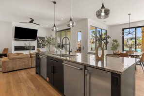 A modern kitchen with a large island, stainless steel appliances, pendant lighting, and a flat-screen TV. - Lagoon Landing: Private Pool + Beach/Lagoon Front (St. George)