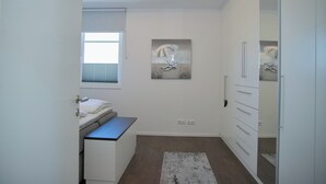 Un dormitorio con cama, escritorio, armario, ventana y un cuadro en la pared.
