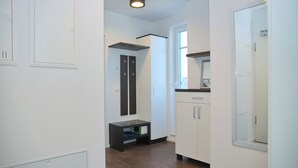 Un pasillo con suelo de madera, paredes blancas, un banco negro y un armario blanco con un espejo.