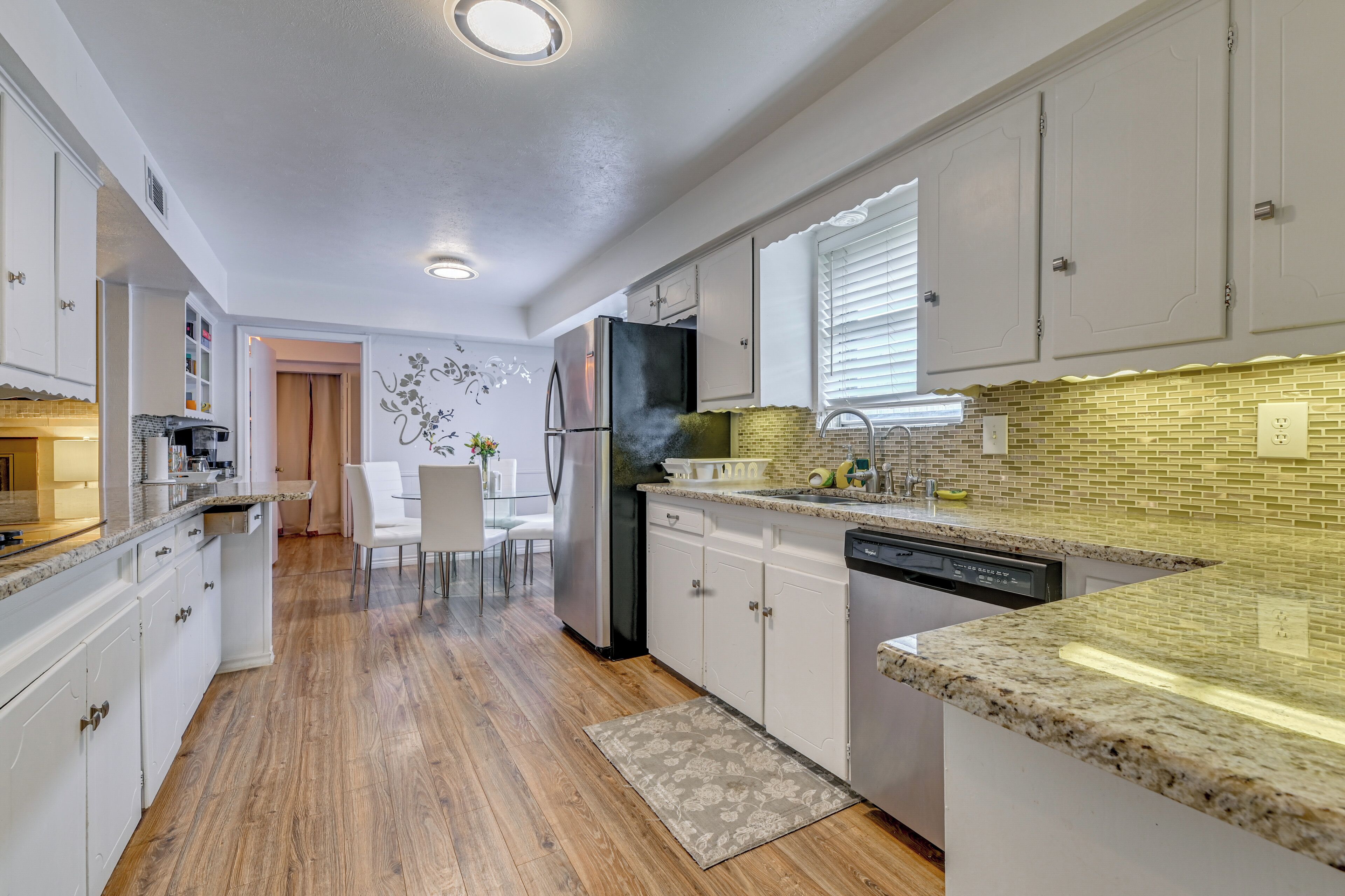 A modern kitchen with white cabinets, a granite countertop, and a brick backsplash.