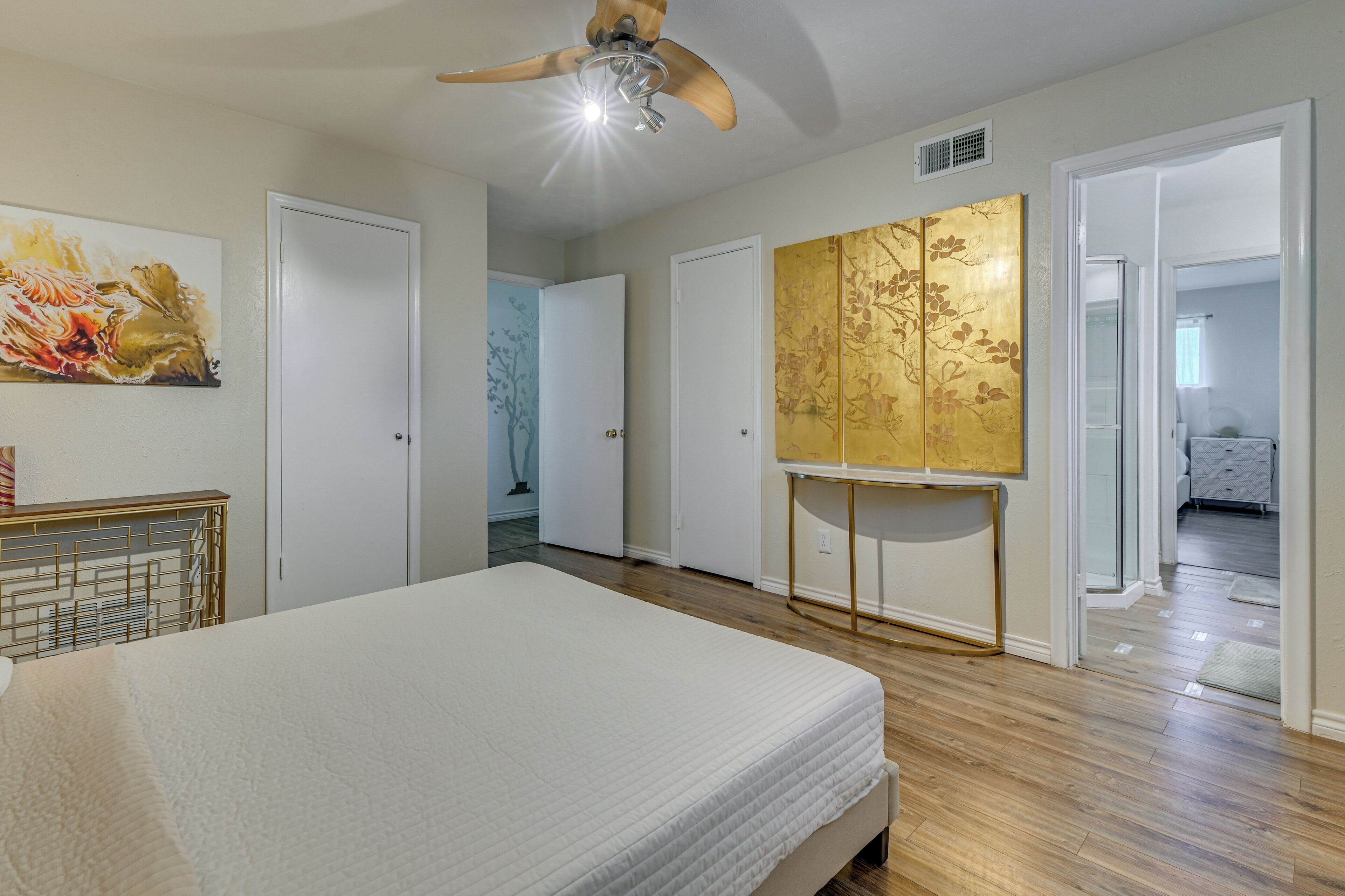 A bedroom with a bed, a ceiling fan, and a painting on the wall.