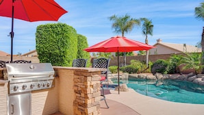 An outdoor barbecue area with a grill, stone pillar, and red umbrella. - Game Room, Backyard Oasis! Glendale Group Getaway (Glendale)