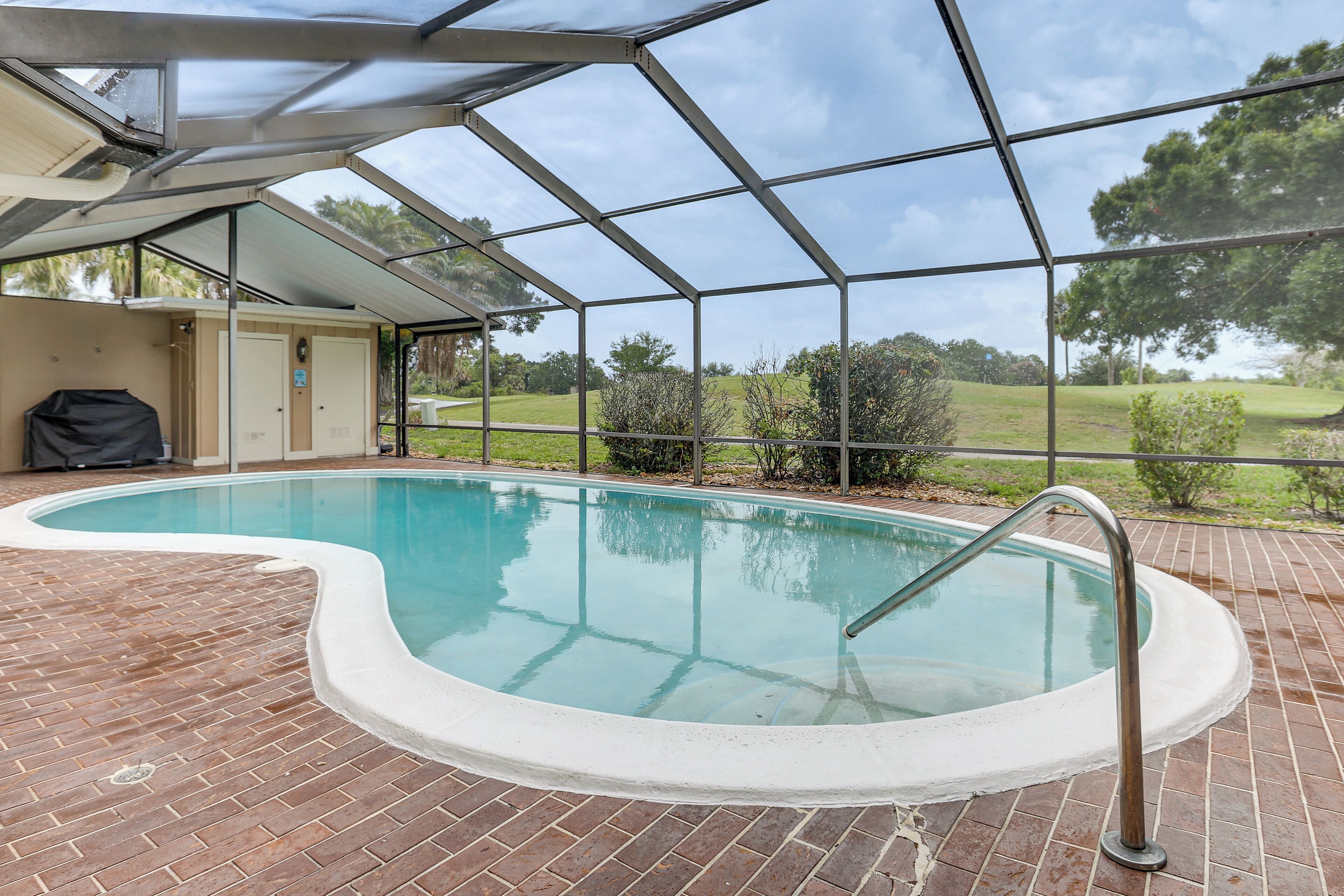 A swimming pool with a covered area, brick flooring, and a view of the surrounding landscape.