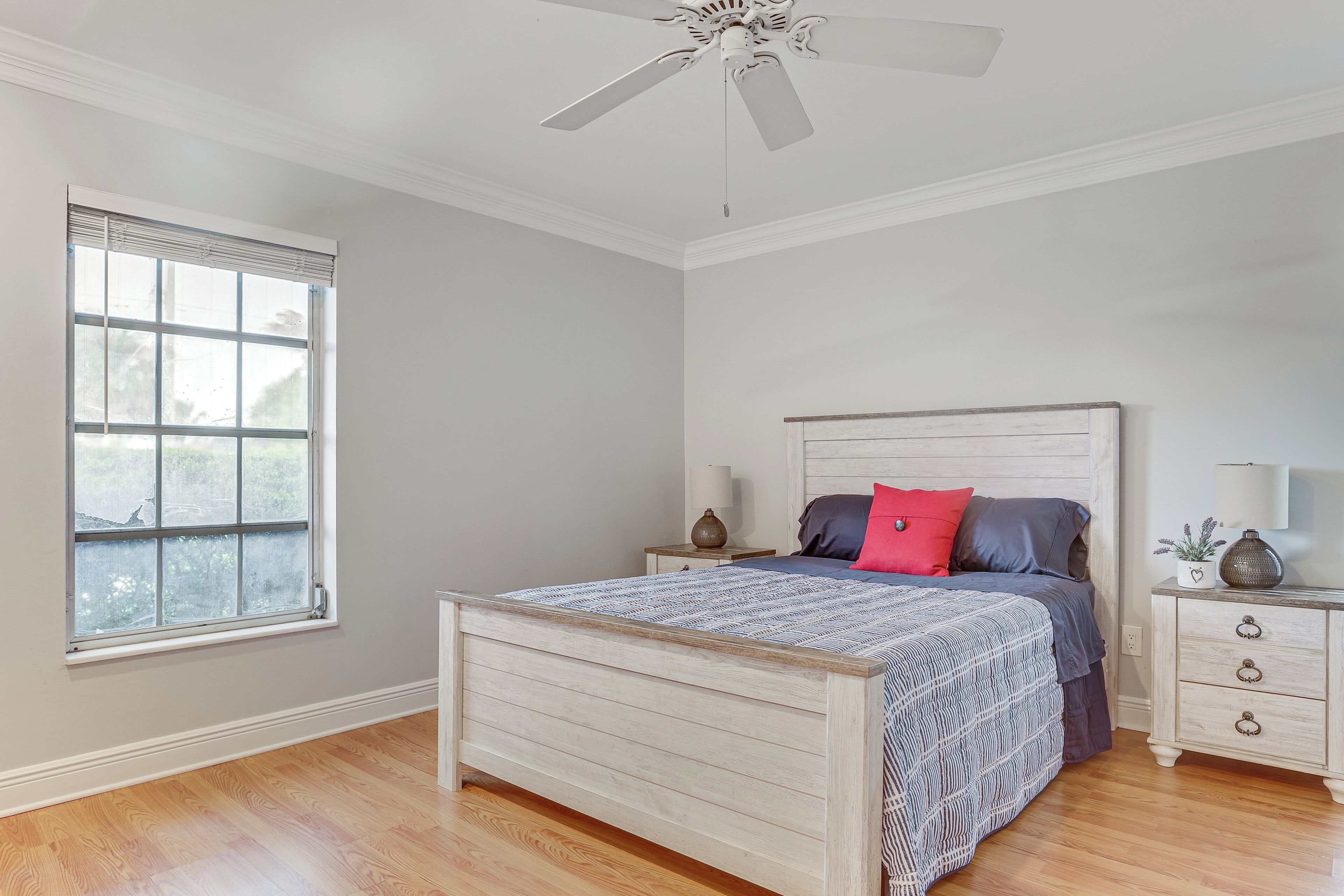 A bedroom with a bed, a nightstand, a dresser, a ceiling fan, and a window.