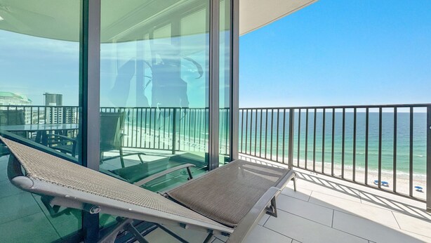 Een balkon met een glazen hekwerk, een lounge stoel en uitzicht op de oceaan.