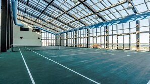 Un court de tennis intérieur doté d’un toit en verre, de bancs et offrant une vue sur l’extérieur.