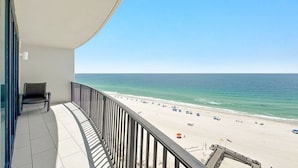 Een balkon met uitzicht op een strand, een stoel en een hekwerk.
