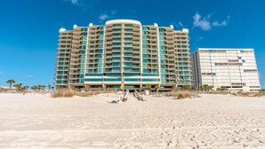 Een strandhotel met een gebogen gevel, meerdere balkons en een zandstrand op de voorgrond.