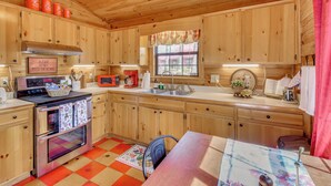 A wooden cabin kitchen with a stove, microwave, sink, and cabinets.