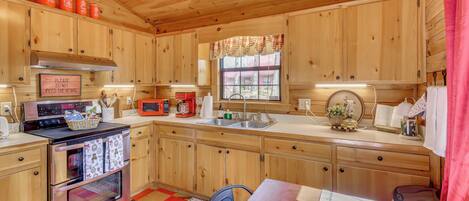 A wooden cabin kitchen with a stove, microwave, sink, and cabinets.