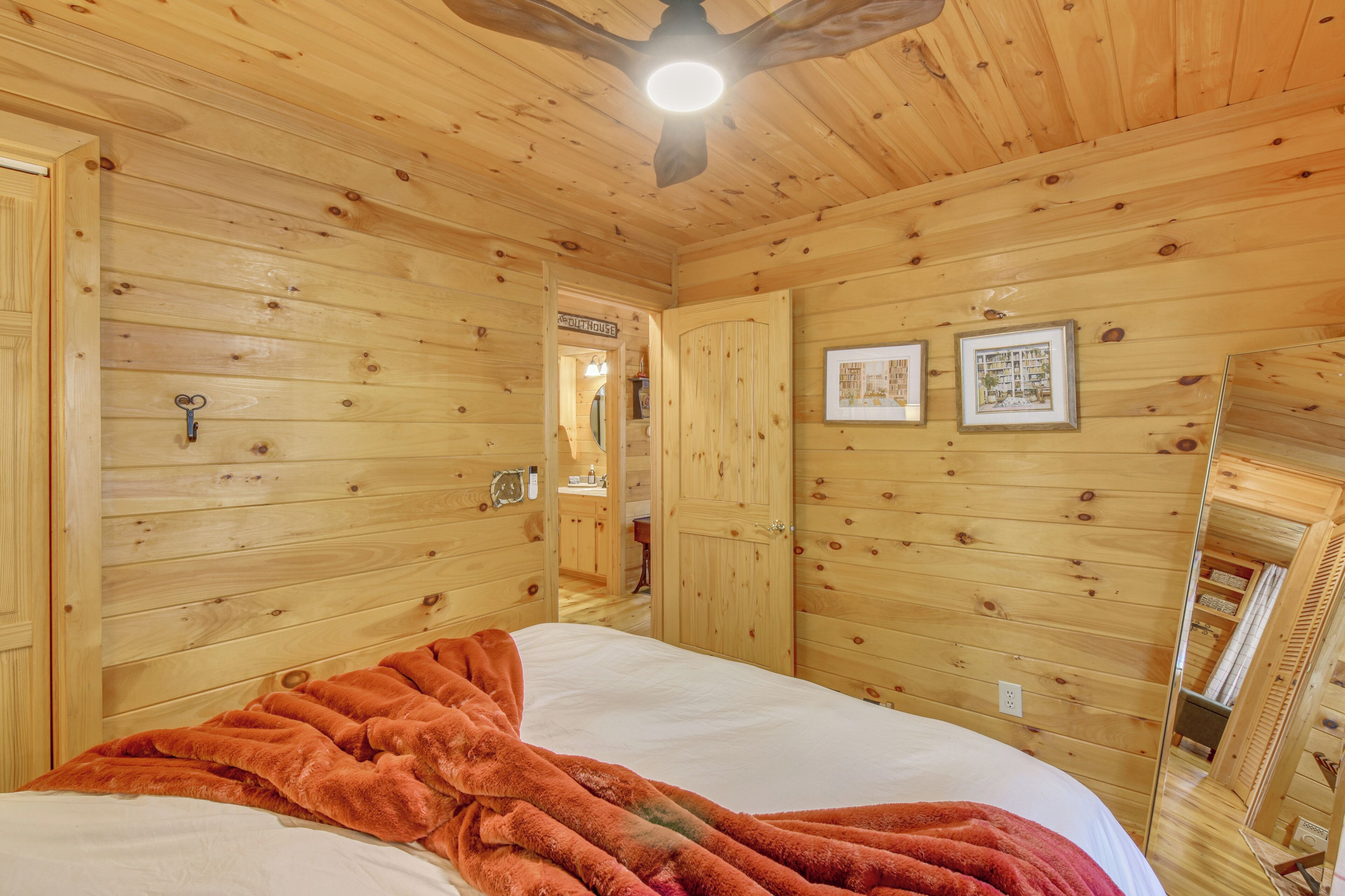 A wooden-paneled room with a bed, a ceiling fan, and framed pictures on the wall.