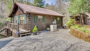 A rustic log cabin with a wooden deck, a small garden, and a gravel driveway.