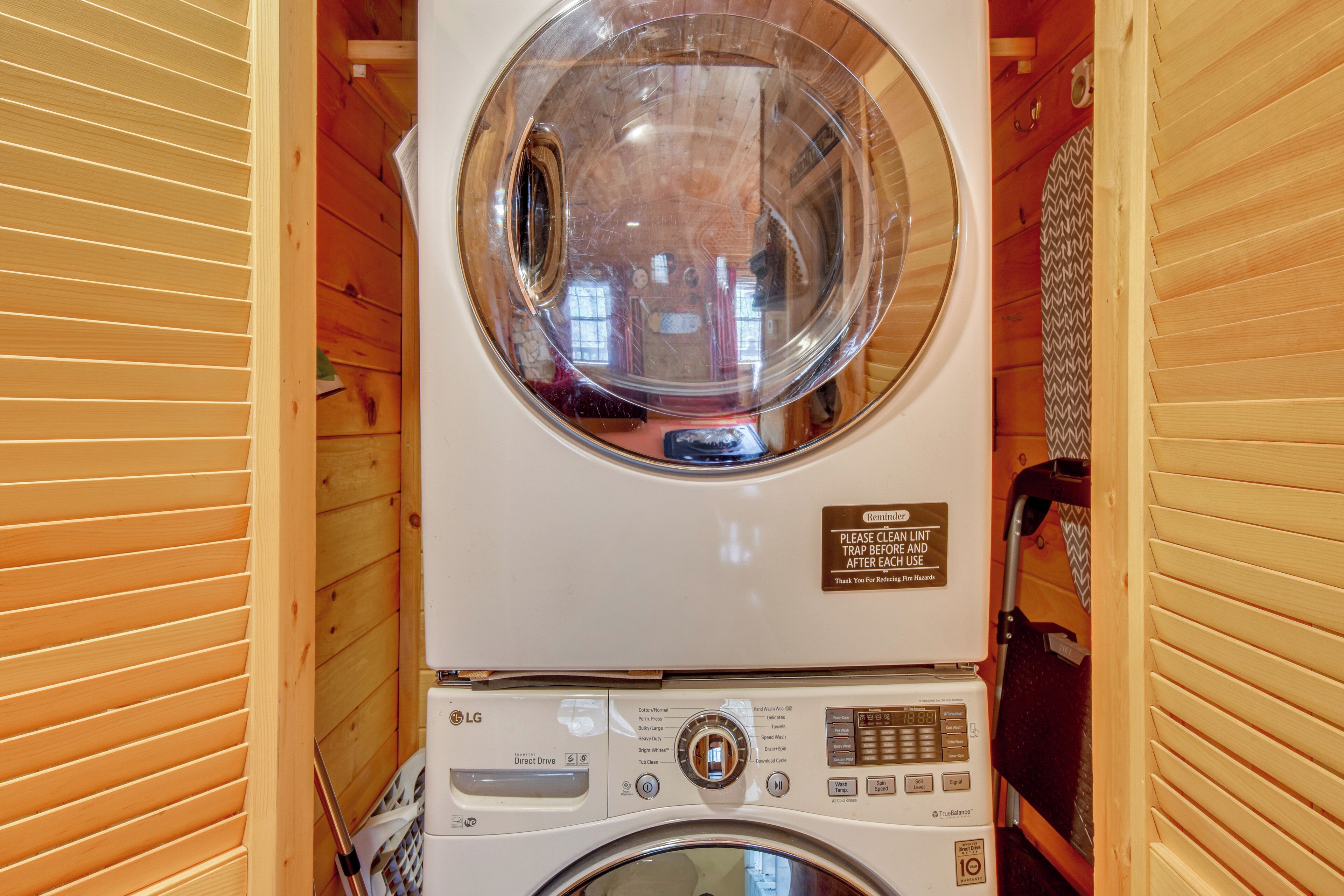 Une petite buanderie aux murs en bois, équipée d’un lave-linge et d’un sèche-linge à chargement frontal, d’un miroir rond et d’un panneau de signalisation de sécurité.