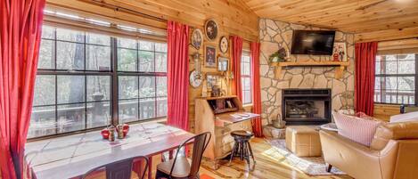 A cozy cabin interior with a wooden ceiling, stone fireplace, dining table, and leather sofa.