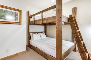 Een stapelbed met een houten frame, witte beddengoed en een ladder.