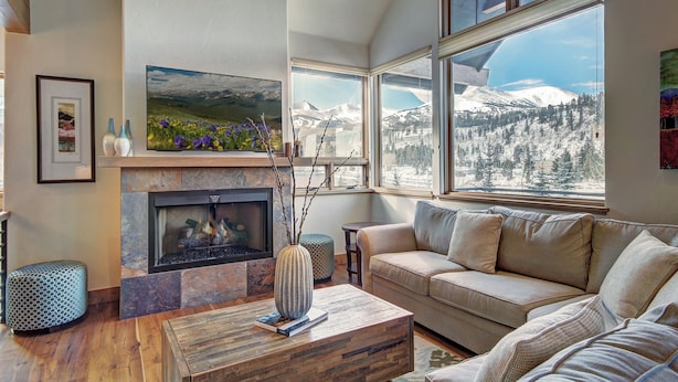 Un salon avec une cheminée, un canapé, une table basse et de grandes fenêtres donnant sur la montagne.