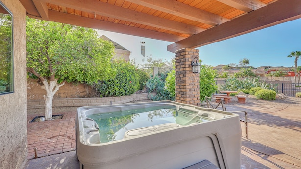A hot tub under a wooden pergola, surrounded by a brick patio, with a view of a house and greenery. - Quiet Home w/ Spacious Yard in Lake Havasu City (Lake Havasu City)