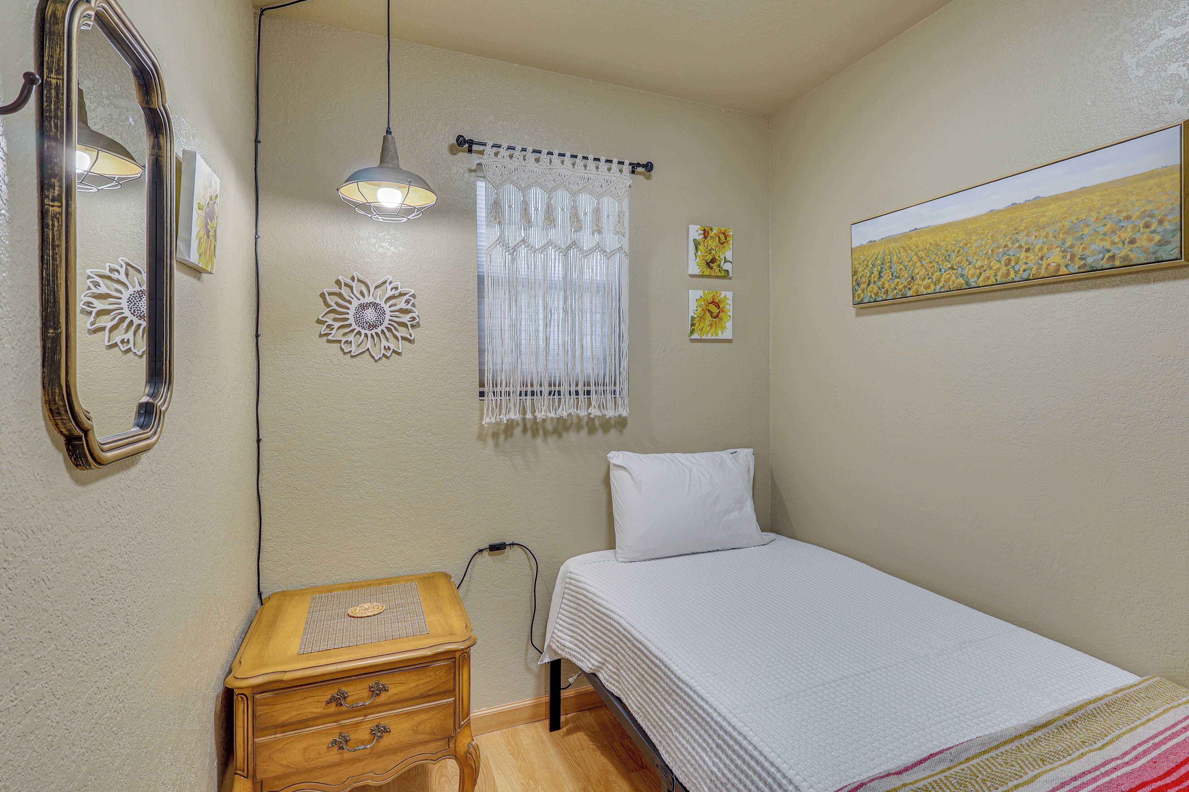 Ein Schlafzimmer mit Bett, Nachttisch, Spiegel, Hängelampe, Vorhang und Wandbild.
