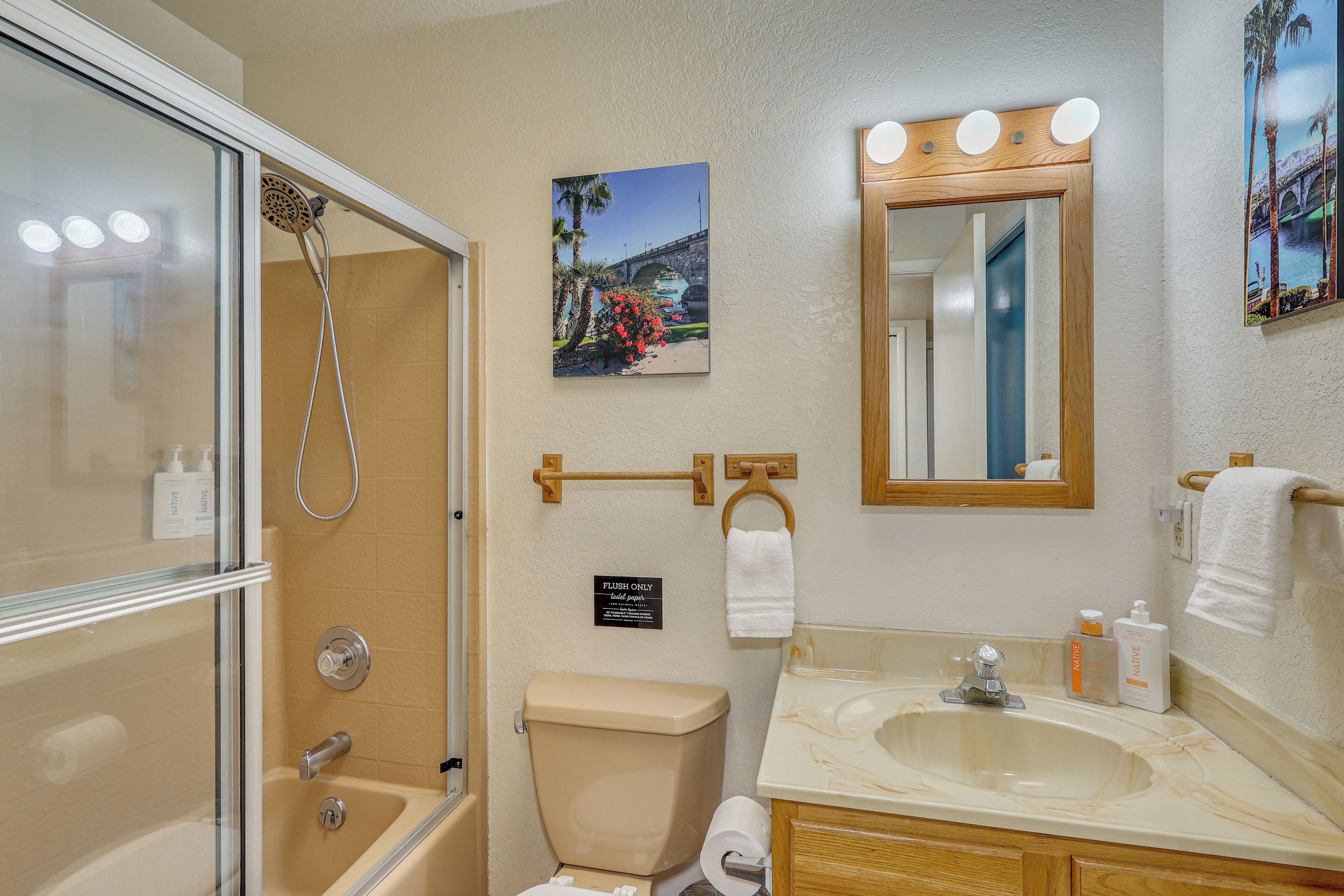 A bathroom with a shower, toilet, sink, and a mirror with lights.