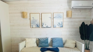 Una cama blanca con tres almohadas, una manta azul y una pared con tres obras de arte enmarcadas.