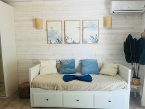 Ein weißes Bett mit drei Kissen, einer blauen Tagesdecke und einer Wand mit drei gerahmten Kunstwerken.