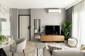Ein modernes Wohnzimmer mit Flachbildfernseher, einem Essbereich mit Tisch und Stühlen sowie einer großen Kübelpflanze.