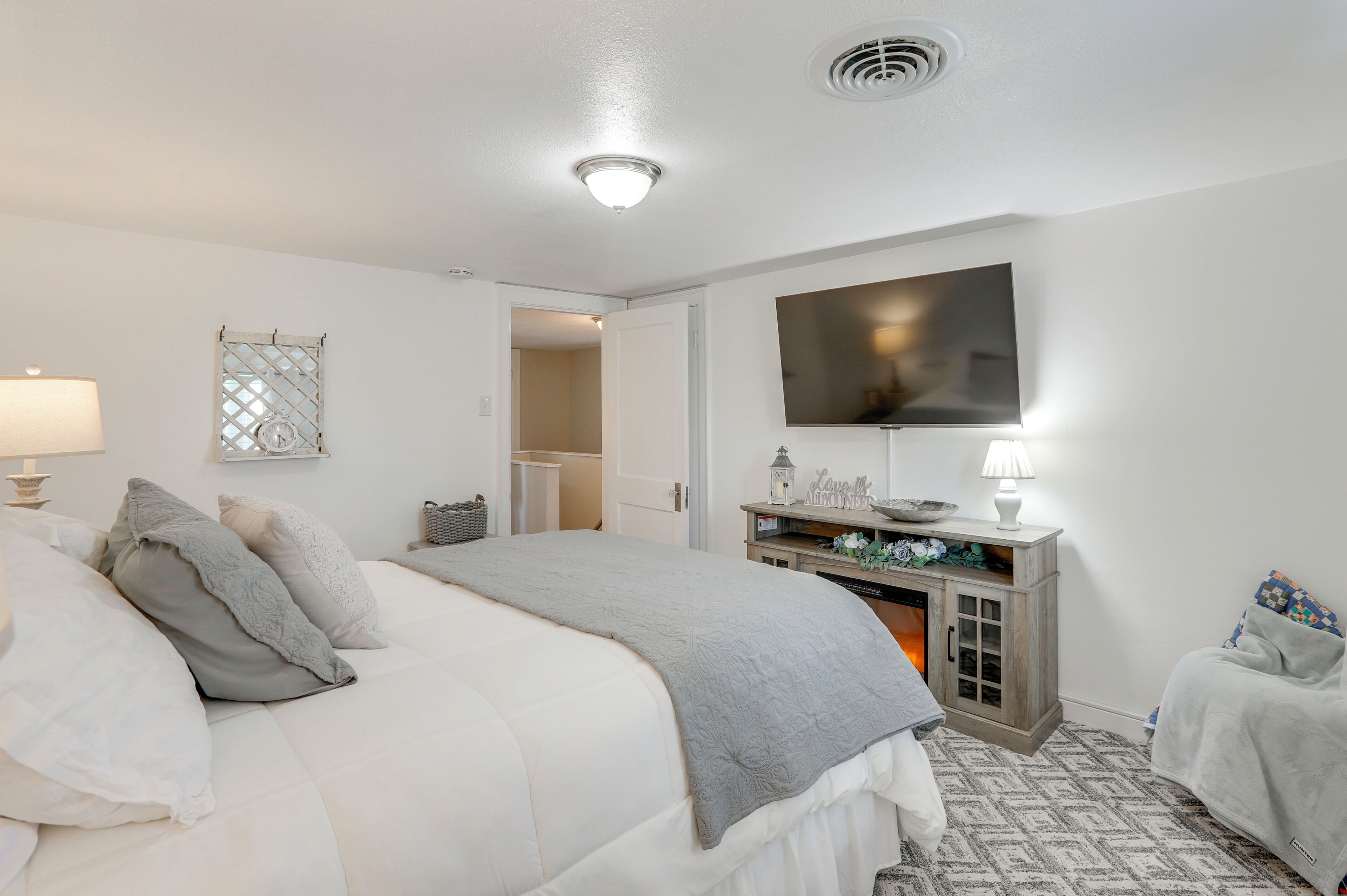 Un dormitorio con cama, lámparas de noche, televisor, cómoda y una puerta que da a otra habitación.