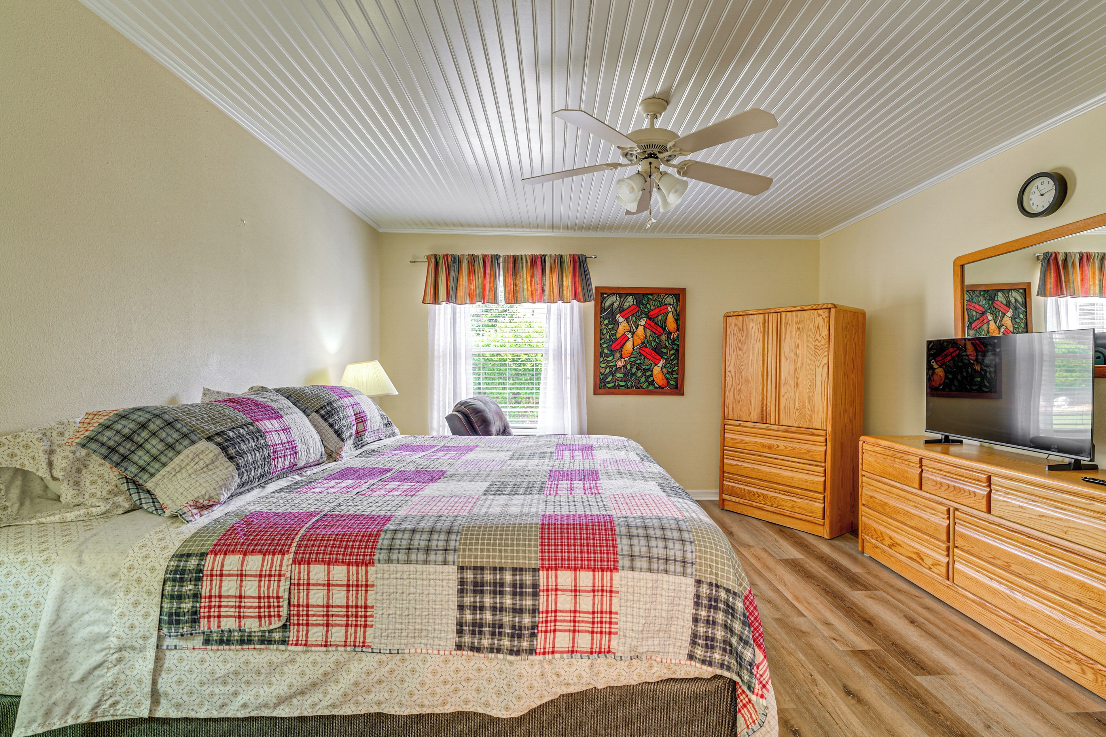 A bedroom with a bed, a ceiling fan, a television, a wardrobe, and a window with curtains.
