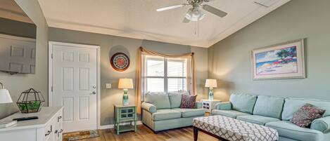 A living room with a ceiling fan, a couch, a coffee table, and a door.