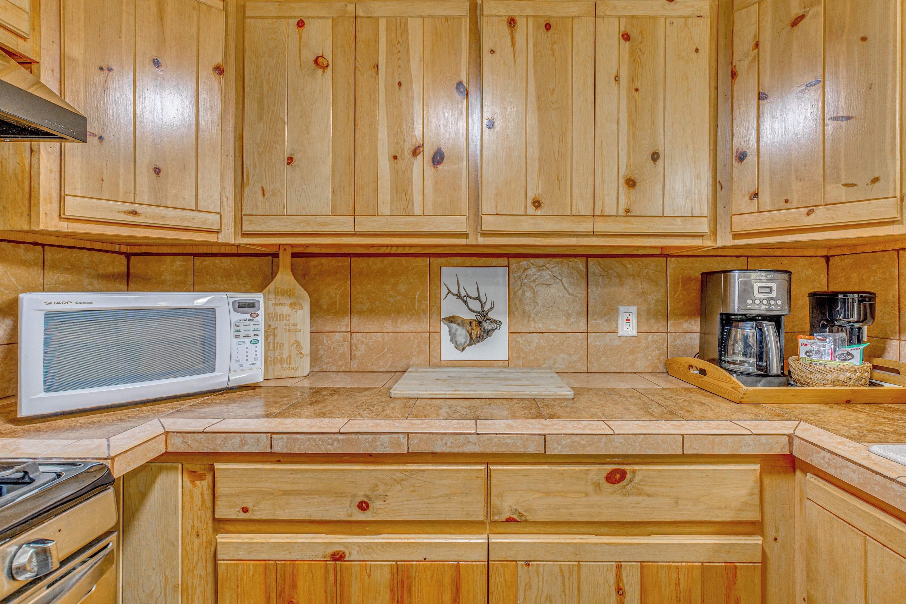 A kitchen with wooden cabinets, a microwave, a coffee maker, and a deer head artwork.