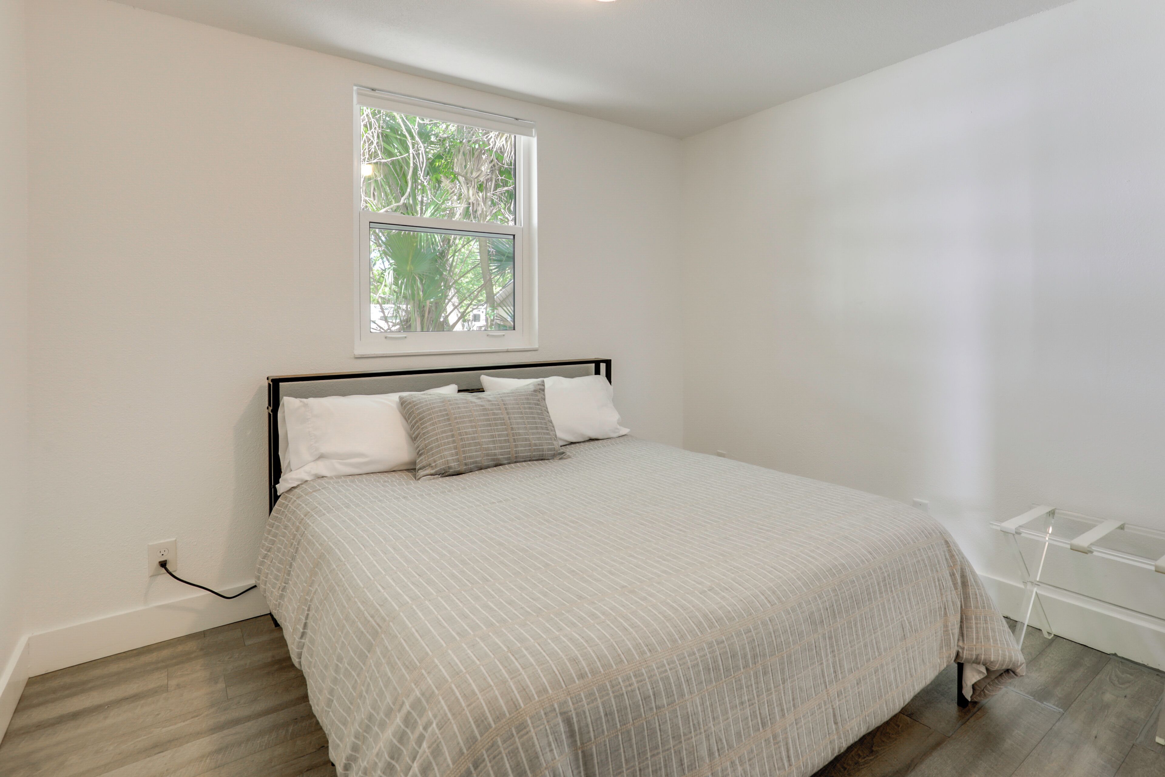 Un dormitorio con cama, ventana y pared blanca.