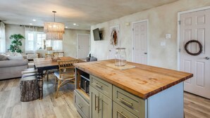 A kitchen with a wooden island, dining table, chairs, and a hanging light fixture.