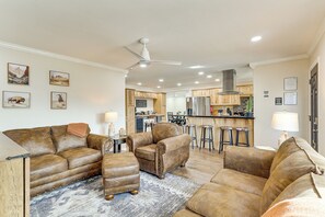 A living room with leather sofas, a coffee table, and a rug. There is a kitchen in the background with wooden cabinets and a bar area. - Outdoor Entertainment Area! Lake Havasu City Home (Lake Havasu City)