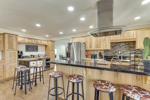 A kitchen with wooden cabinets, a stainless steel refrigerator, a bar area with stools, and a sign that reads 'COFFEE COCKTAILS.' - Outdoor Entertainment Area! Lake Havasu City Home (Lake Havasu City)