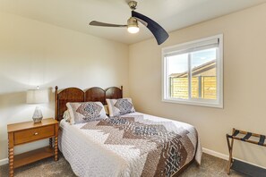 Ein Schlafzimmer mit Bett, Nachttisch, Lampe, Deckenventilator und Fenster.