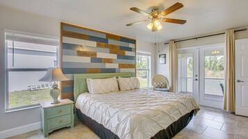 A bedroom with a bed, a nightstand, a ceiling fan, a window with blinds, and a door.