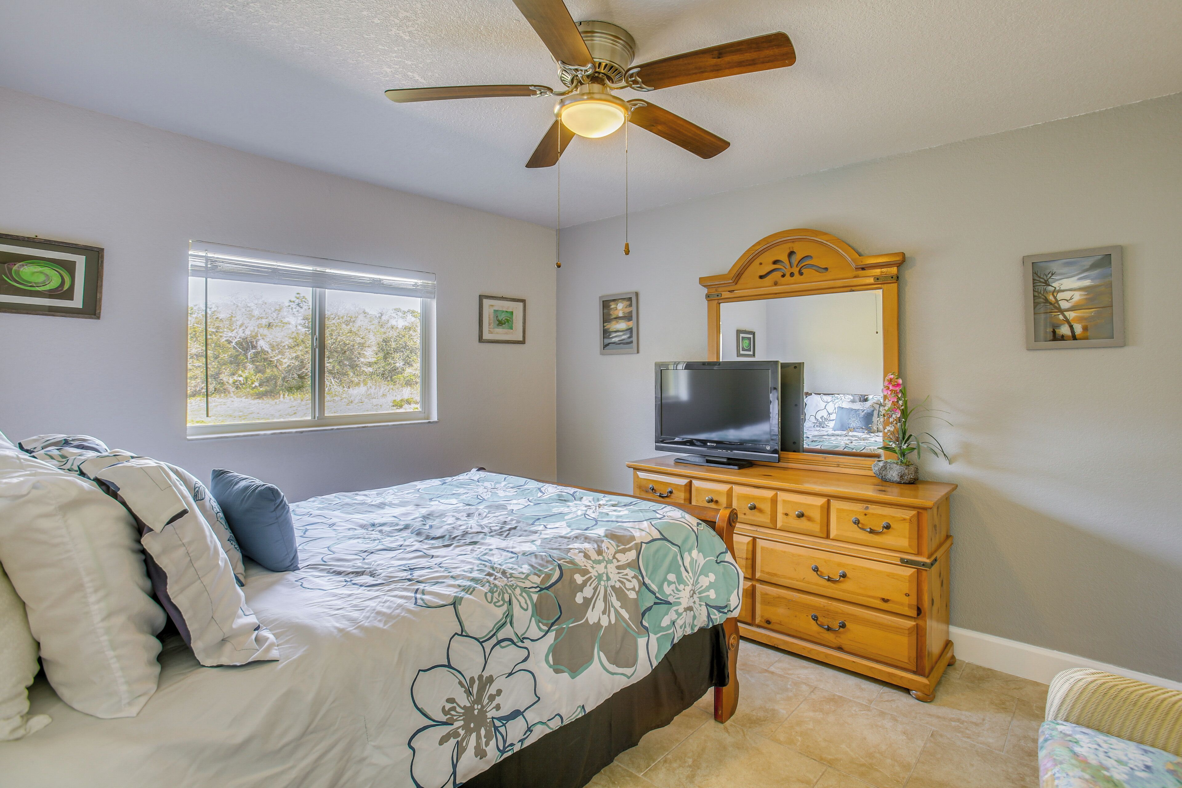 A bedroom with a bed, a dresser, a ceiling fan, a television, and a window.