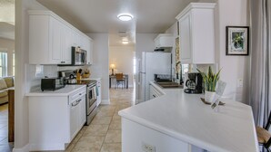 Cozinha moderna com armários brancos, uma ilha central e uma área de refeições ao fundo.