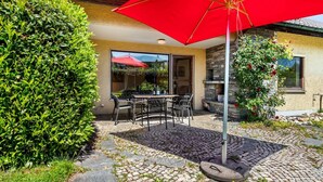 Eine Terrasse mit Tisch und Stühlen, einem roten Sonnenschirm und einem gepflasterten Weg.