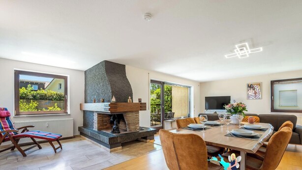 Ein modernes Wohnzimmer mit Kamin, Essbereich und großen Fenstern.