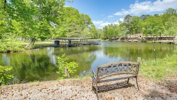 A bench by a calm lake with a wooden deck and a gazebo in the background.