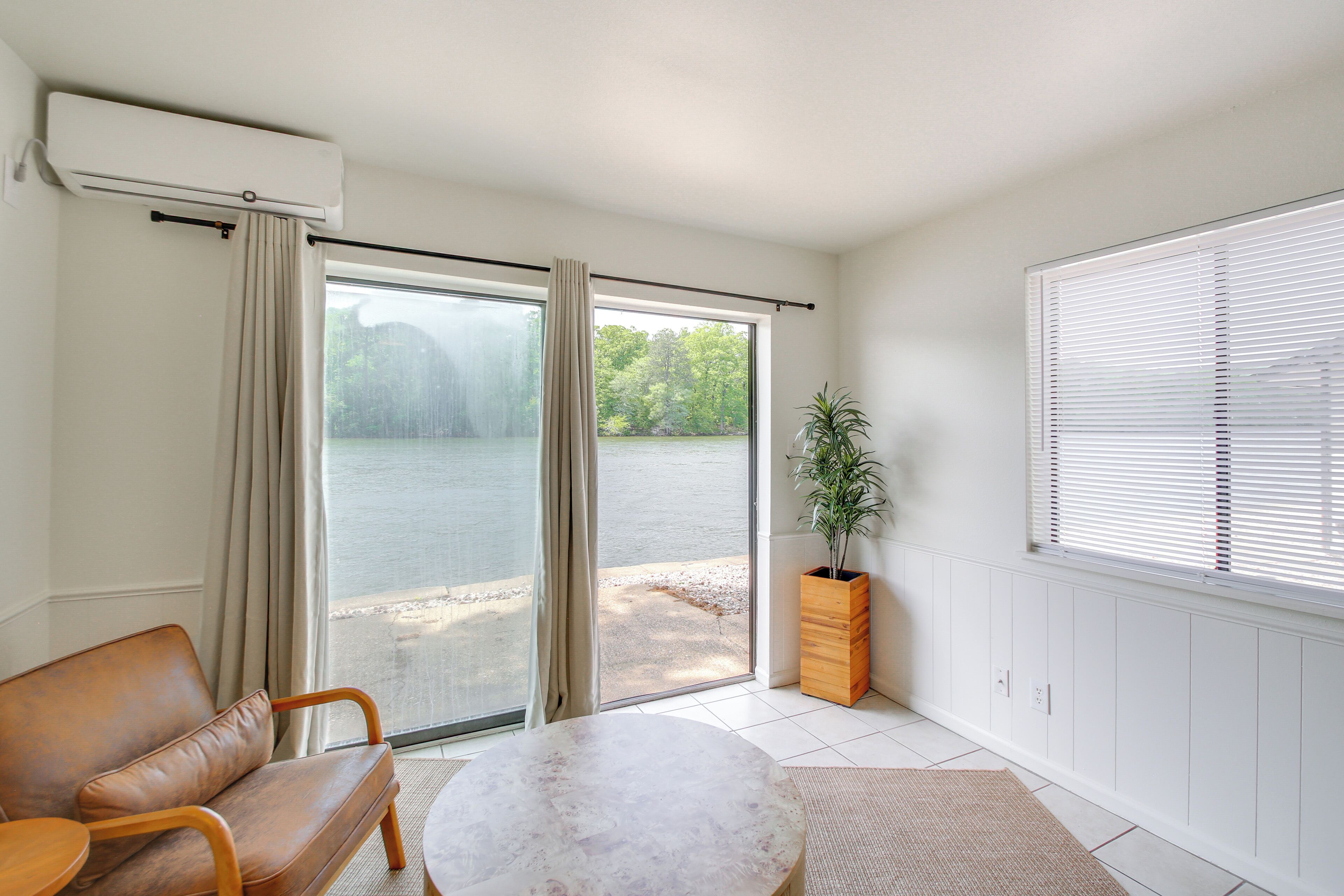 A room with a sliding glass door to a lake, a brown leather sofa, a round table, and a potted plant.