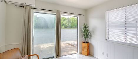 A room with a sliding glass door to a lake, a brown leather sofa, a round table, and a potted plant.