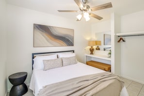 A bedroom with a bed, a ceiling fan, a bedside table, a lamp, a mirror, and a coat rack.