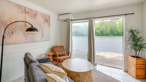 A modern living room with a sofa, a round coffee table, a chair, a lamp, and a large window with a view of a body of water. - Waterfront Couples Retreat in Hot Springs! (Hot Springs)